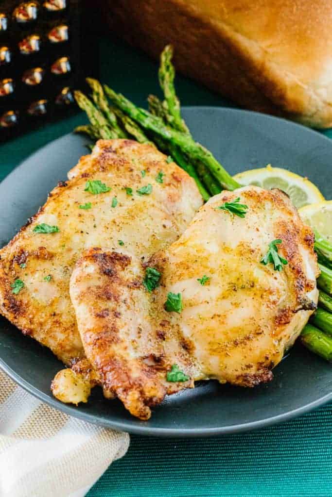 Cooked air fryer chicken thighs next to cooked asparagus stalks and lemons on blue plate