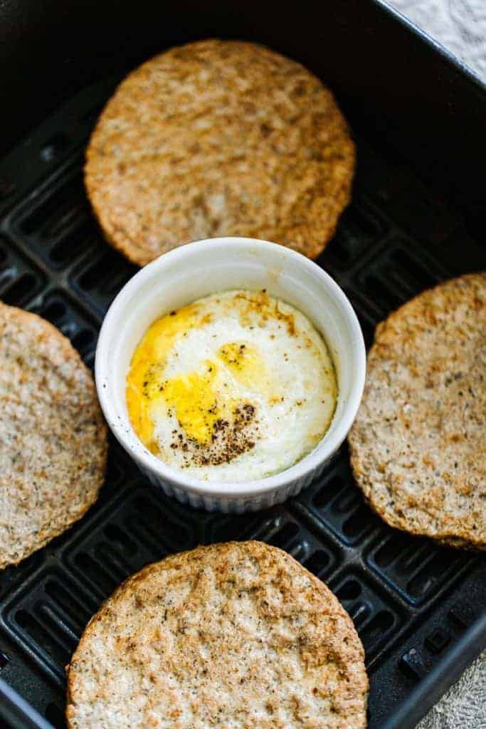 peppered cooked air fryer egg in white ramekin in instant pot surrounded by four cooked air fryer sausage patties