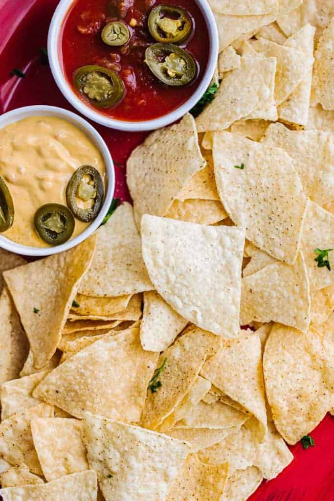 top view of air fryer tortilla chips in red bowl next to salsa and cheese topped with jalapeños