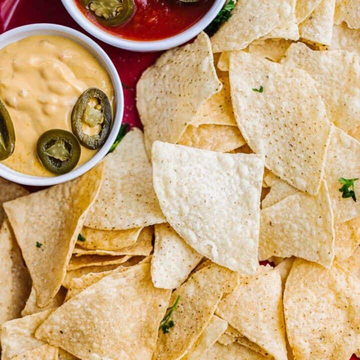 top view of air fryer tortilla chips in red bowl next to salsa and cheese topped with jalapeños