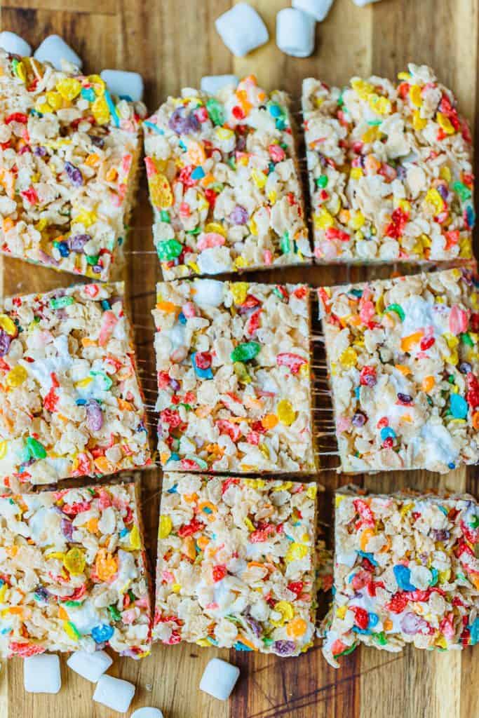 top view of fruity pebble rice krispies cut into nine squares on a wood board surrounded by marshmallows