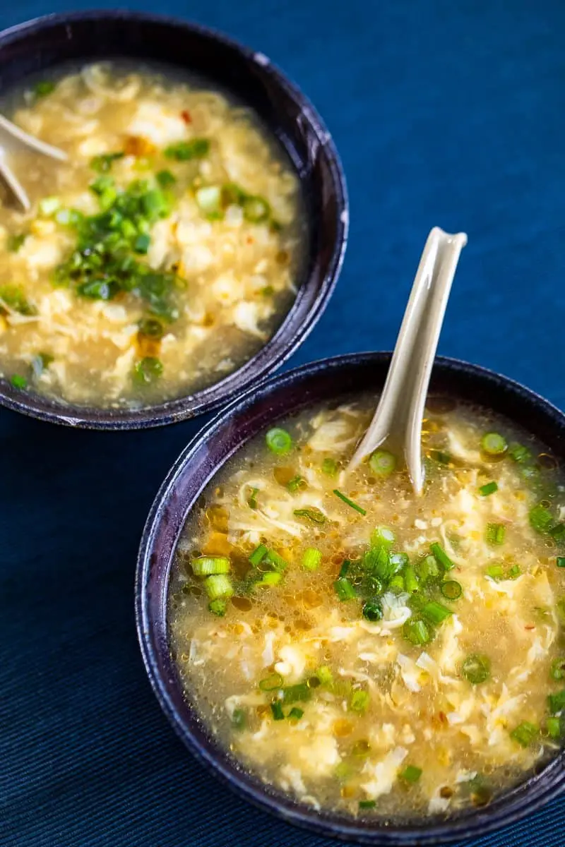 two bowls of egg drop soup on a blue placemat