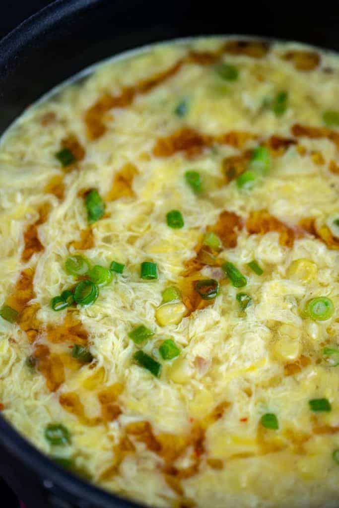 closeup of egg drop soup with a drizzle of dark sesame oil and green onions
