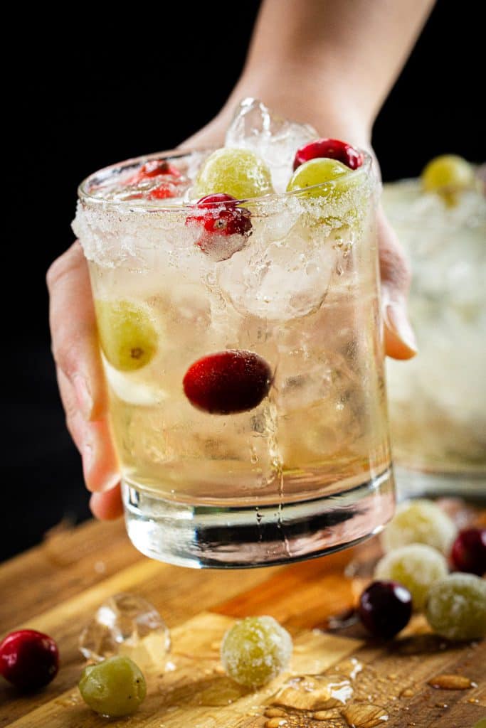 a hand holding a glass of white grape mocktail with cranberries