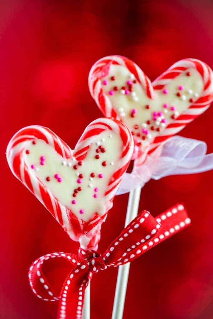 Closeup of two candy cane heart pops tied with a ribbon on a red background