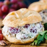chicken salad sandwich next to red grapes and pecans on a wood board