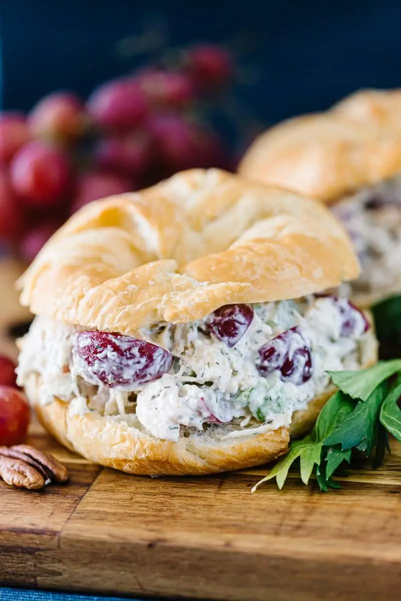 chicken salad sandwich next to red grapes and pecans on a wood board