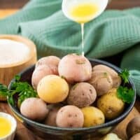 salt potatoes in a blue bowl while a white spoon drizzles butter on top