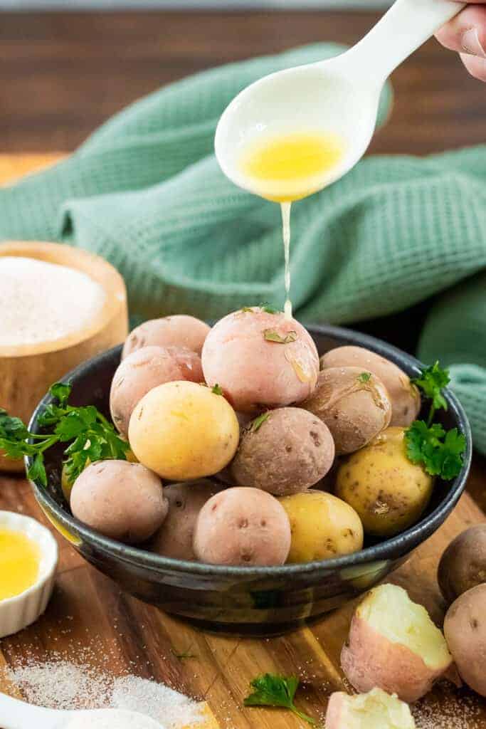 salt potatoes in a blue bowl while a white spoon drizzles butter on top