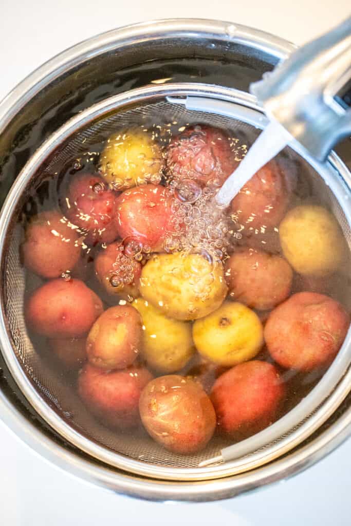 an Instant Pot with a steamer basket full of potatoes with water flowing into the pot