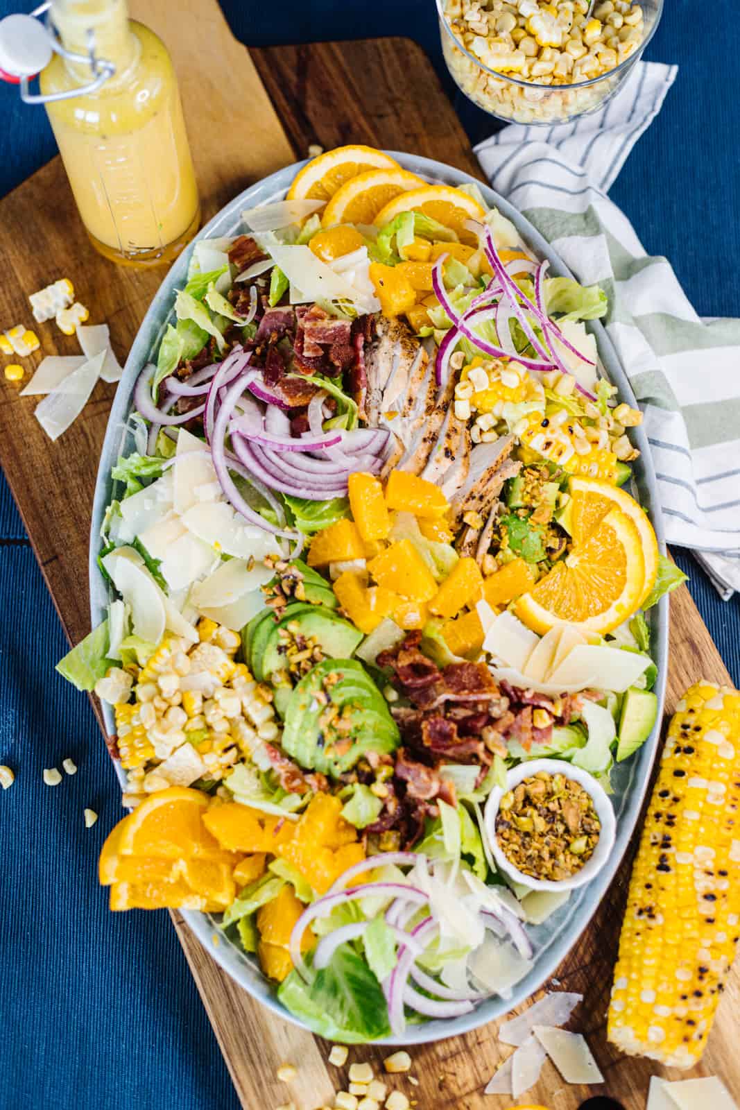 Top view of assembled catana salad in white bowl on cutting board and blue cloth surrounded by cobb corn and vinaigrette