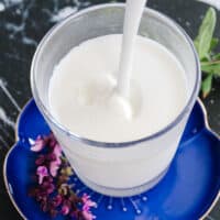 top view of instant pot yogurt in glass cup with spoon in yogurt on a blue plate next to pink flowers