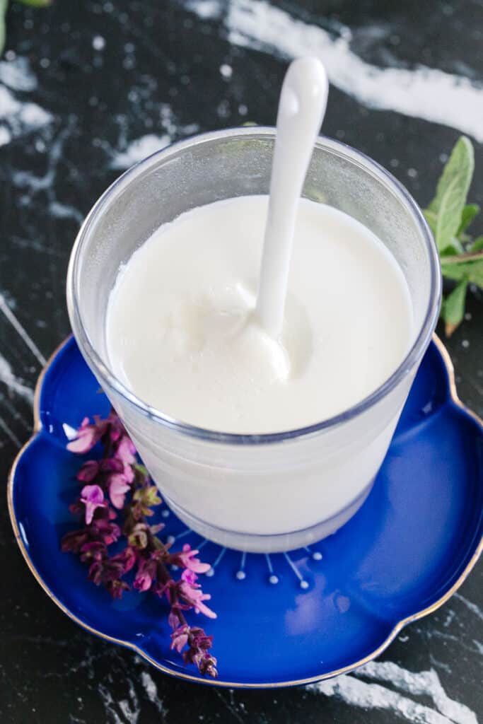 top view of instant pot yogurt in glass cup with spoon in yogurt on a blue plate next to pink flowers