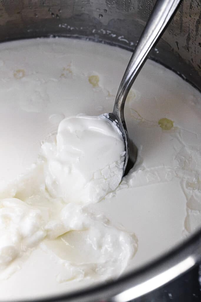 close up of instant pot yogurt being scooped with a spoon inside the instant pot