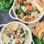 top view of two bowls of zuppa toscana soup in white bowls next to bread and greens on a black board