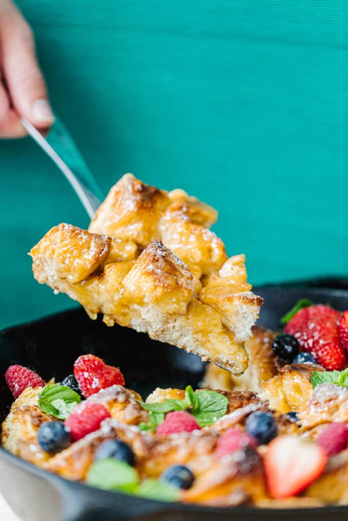 fork lifting out a slice of bread pudding from cast iron skillet