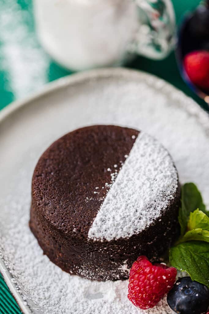 small round chocolate cake half dusted with powdered sugar, next to berries