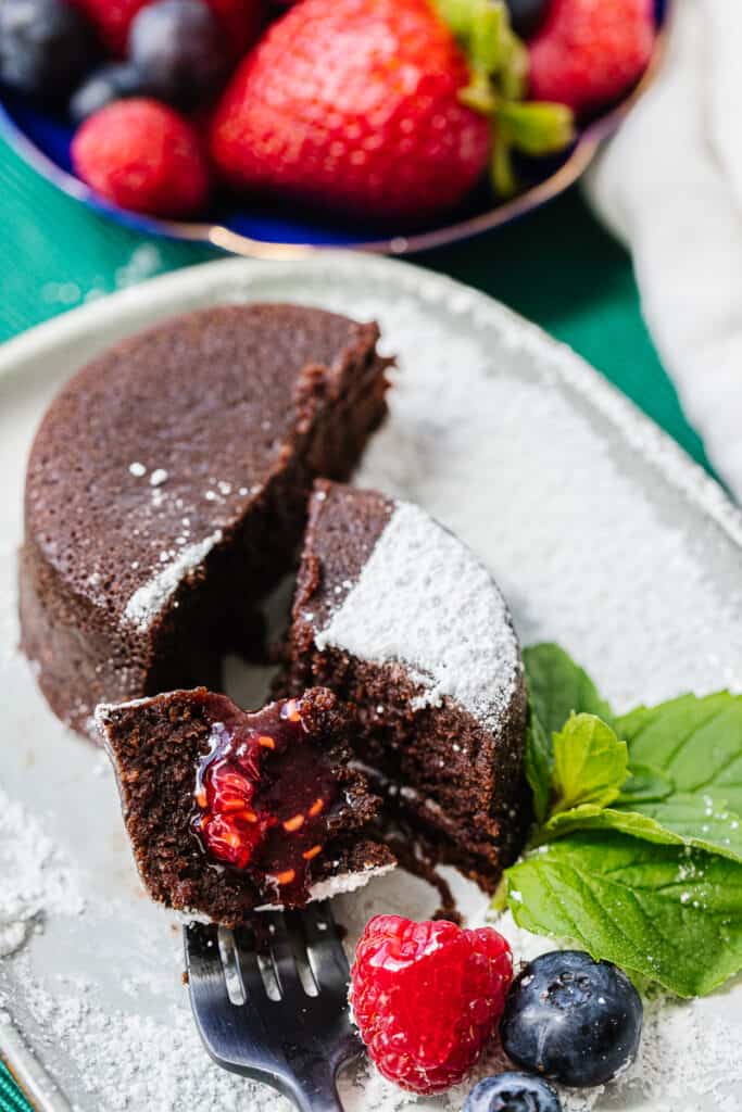 fork taking piece of chocolate cake topped with a raspberry from sliced chocolate cake
