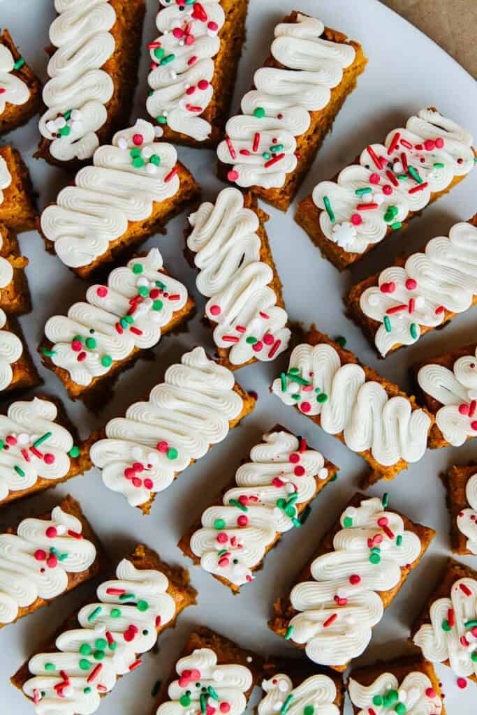 top view of sliced pumpkin bars, topped with white cream cheese frosting and green, white, and red sprinkles.