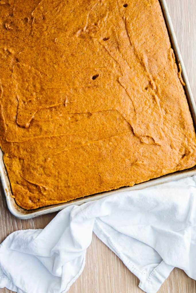 top view of baked pumpkin bars in a sheet pan on a table next to a white cloth