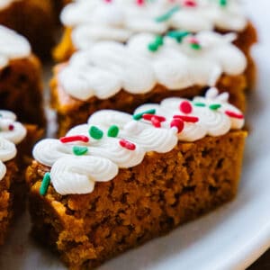 close up of a sliced pumpkin bar, topped with white cream cheese frosting and green, white, and red sprinkles.